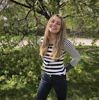 a young woman in a striped shirt standing in front of a tree